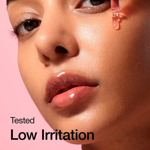 Close-up of a person's face with a droplet of ANUA serum on their cheek against a pink background, labeled 'Tested Low Irritation'.
